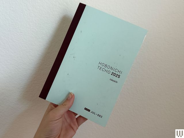 Hand holding up a small planner book with a blue cover