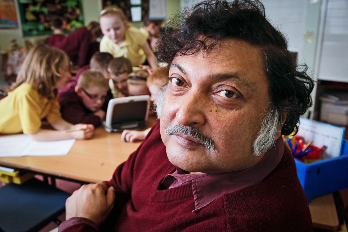 closeup photo of man in classroom with students looking at a tablet