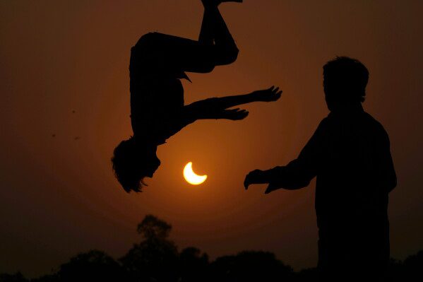 The partial solar eclipse is framed by youngsters jumping on a trampoline in the outskirts of Lahore, Pakistan, Oct. 25, 2022. (AP Photo/K.M. Chaudary, File)