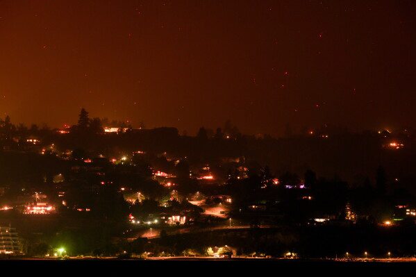 Hot spots from the Bald Range wildfire burn on the mountainside above houses in Summerland, British Columbia, late Saturday, Aug. 8, 2026. (Darryl Dyck/The Canadian Press via AP)