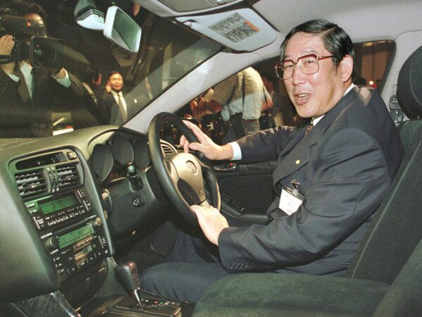 Hiroshi Okuda, then, president of Toyota Motor Corp., smiles as he sits at the steering wheel of the "Aristo," Toyota's remodeled sports sedan during a press conference at a Tokyo hotel, Aug. 27, 1997. (AP Photo/Shizuo Kambayashi, File)