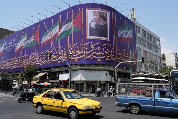 Vehicles drive past a billboard showing a photo of the late Iranian Supreme Leader Ayatollah Ali Khamenei, right, greeting the late Hamas leader Ismail Haniyeh, and Iranian and Palestinian flags, at an intersection in downtown Tehran, Iran, Saturday, Aug. 1, 2026. (AP Photo/Vahid Salemi)