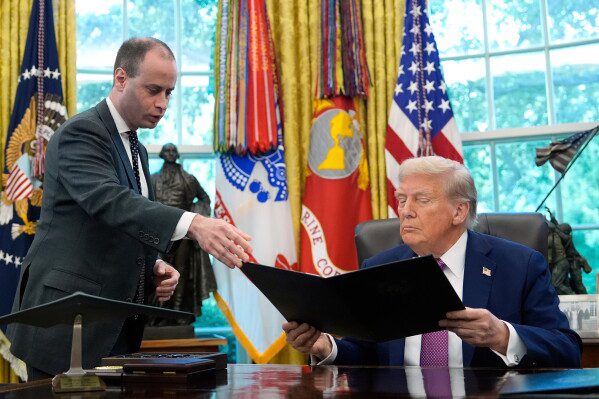 White House staff secretary Will Scharf, left, hands President Donald Trump an executive order to sign in the Oval Office of the White House, Sept. 5, 2025, in Washington. (AP Photo/Alex Brandon, File)